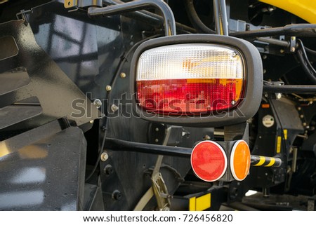Close up of tractor headlight and cataphot, selective focus. Tractor red and orange lights against the background of the details of the car body. Design and technology