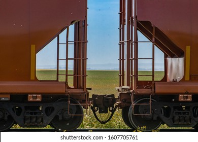 Close up of train coupler connecting two red wagons of a Canadian freight or cargo train. Green fields and blue sky in the background.