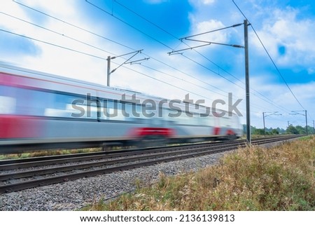 Close up of a train with overhead electrification speeding through English countryside with motion blur on a sunny day