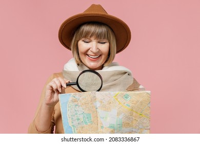 Close Up Traveler Tourist Mature Elderly Senior Lady Woman 55 Years Old Wear Brown Shirt Hat Scarf Hold Examine Map With Magnifying Glass Isolated On Plain Pastel Light Pink Background Studio Portrait