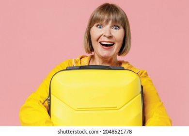 Close Up Traveler Tourist Shocked Mature Elderly Woman 55 Years Old Wears Yellow Raincoat Hold Carry Suitcase Bag Keep Mouth Wide Open Isolated On Plain Pastel Light Pink Background Studio Portrait