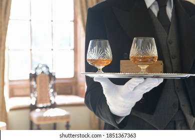 Close up of a tray containing two glasses of whiskey carried by a butler inside a luxurious house on a bright, sunny day