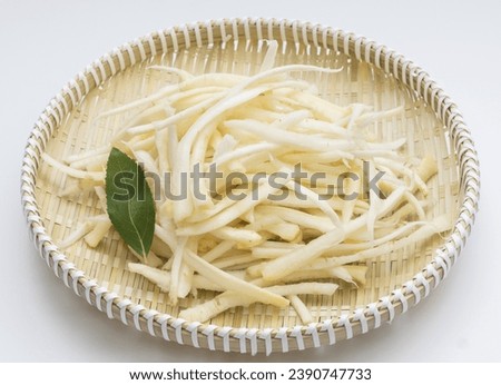 Close up of trimmed raw balloon flower roots with a green leaf on bamboo basket and white floor, South Korea

