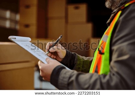 Close up of truck driver taking notes while going through delivery list.