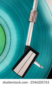 Close up of turntable needle on a vinyl record. Turntable playing vinyl. Needle on rotating cyan vinyl.