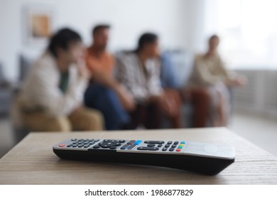 Close Up Of TV Remote On Table With Blurred Group Of People Watching Movies At Home In Background, Copy Space