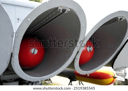 Close up of twin red spherical objects in gray conical mounts, possibly machinery parts blurred green outdoor background suggesting an industrial or mechanical context military concept war torpedos