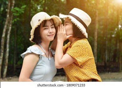 Close Up Of Two Asian Girls Dressed In Hat Weave Whispering A Secret Ear At Park In The Outdoors.