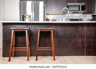 Close up of two bar stools at a kitchen bar, with a white quartz countertop. Stainless steel appliances behind.