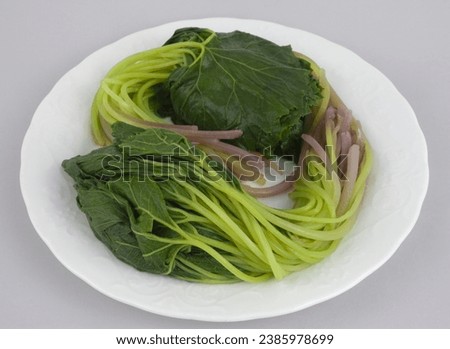 Close up of two bundles of blanched butterbur leaf with stem on white square dish and gray floor, South Korea
