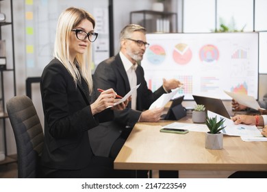 Close up of two business colleagues at the table in modern office room, working together with digital tablet and papers. Focus on young blond woman, smiling at camera while making notes. - Powered by Shutterstock