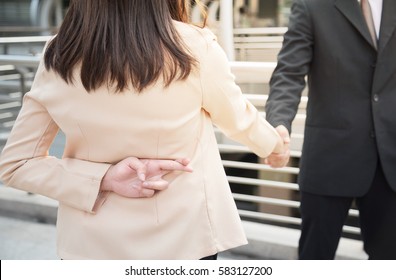 Close Up Of Two Business People Shaking Hand Making A Deal But Business Woman Holding Crossed Fingers Behind Back, Betray Concept.