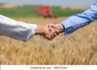 Close up of two businessmen shaking hands on the farmland. Combine harvester working in background