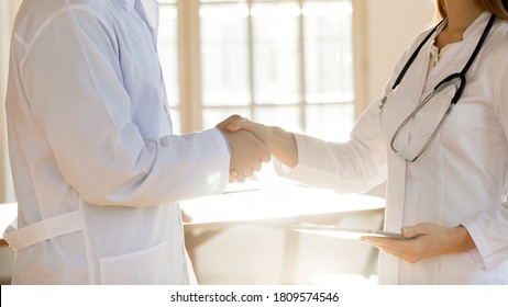 Close up two doctors colleagues shaking hands, greeting, celebrating success, young woman and man wearing white uniform standing in office in hospital, medical staff teamwork concept - Powered by Shutterstock