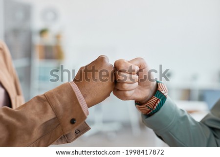 Close up of two ethnic young women fist bumping in office setting, copy space