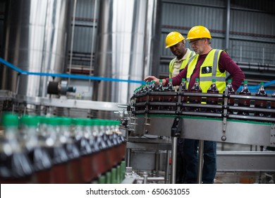 Close up of two factory workers monitoring cold drink bottles at drinks production plant - Powered by Shutterstock