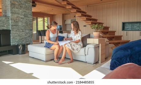 CLOSE UP Two Females Sitting In Living Room And Checking House Building Plans. Young Women Discussing Plans And Considering Energy Flow To Organize And Arrange Home Living Space According To Feng Shui