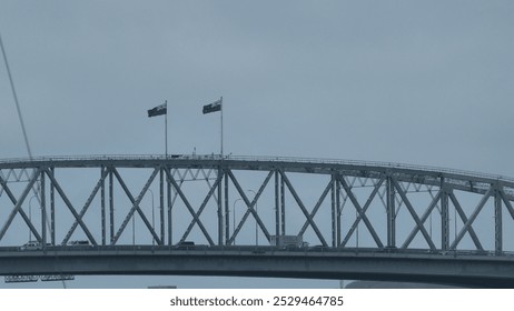 A close up of two flags flying on top of the auckland harbour bridge. october 2024. 