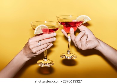 Close up of two hands clinking cocktails against vibrant yellow background in celebration, copy space - Powered by Shutterstock