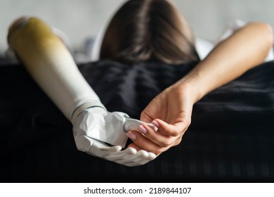 Close Up Two Hands Of Woman With Bionic Arm On Black Bed At Home, Person Lost Her Arm, Girl Artificial Prosthetic Limb