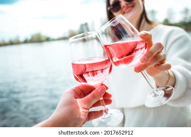 Close up of two happy women cheering with glasses of rose wine and smiling while having picnic. Beautiful and stylish girls best friends drinking wine and laughing. Celebrating some event or birthday - Powered by Shutterstock