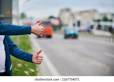 Close up of two man's hands hitchhiking by roadside. Male hands showing thumbs up gesture outdoors on blurred background. Hitchhiking, hitching, auto stop concept.