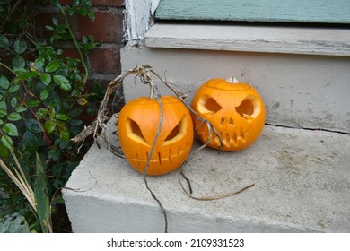 Close Up Of Two Orange Pumpkins With Carved Put  Scary Faces.  The Gourds Are Sitting On A Door Step Outside Of A Family's Home Ready For Halloween