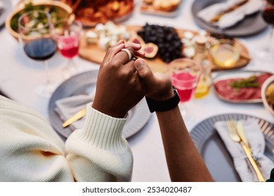 Close up of two people holding hands at dinner table and saying grace during Thanksgiving celebration with friends and family copy space - Powered by Shutterstock