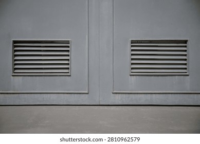 Close up of two rectangular ventilation grilles on a pair of grey painted solid metal double doors.