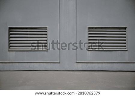Close up of two rectangular ventilation grilles on a pair of grey painted solid metal double doors.