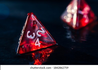 Close up of two red 4 sided dice on a wet slate surface. Focused on the front. Lens flare