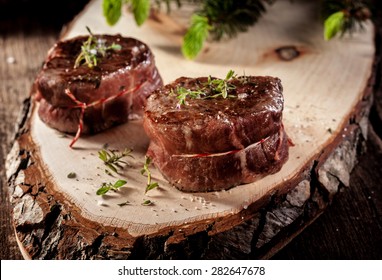 Close Up of Two Roasted Venison Steak Filets Seasoned with Fresh Herbs and Served on Rustic Wood Plank