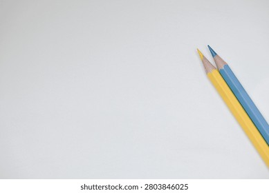 Close up of two sharpened colored pencils in yellow, and blue resting on a plain white surface. Showcasing colorful stationery, creative tools, and minimalist composition ideal for education, art, design, and school concepts.