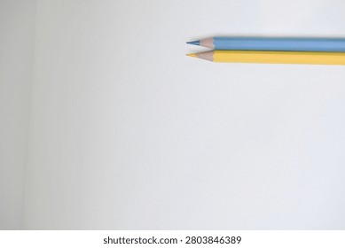 Close up of two sharpened colored pencils in yellow, and blue resting on a plain white surface. Showcasing colorful stationery, creative tools, and minimalist composition ideal for education, art, design, and school concepts.