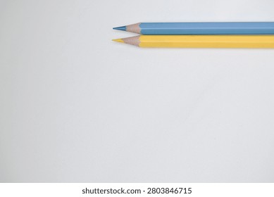 Close up of two sharpened colored pencils in yellow, and blue resting on a plain white surface. Showcasing colorful stationery, creative tools, and minimalist composition ideal for education, art, design, and school concepts.