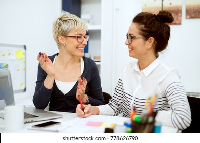 Close up of two smiling stylish business middle aged women working and having a conversation while sitting in the office one next to another.