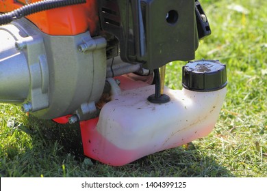 Close Up Two Stroke Motor Engine Of Orange Garden Mowing Machine Trimmer With Red Oil Mix Gas On Green Grass Background