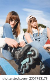 Acercar a dos hermanas rubias adolescentes sentadas ajustando sus patines en línea en un parque. Actividades al aire libre para niños con ejercicio saludable.