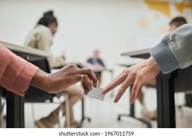 Close Up Of Two Unrecognizable Students Passing Cheat Note While Taking Exam In School, Copy Space