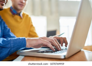 Close up of two unrecognizable students using laptop at desk in college, focus on hands typing on keyboard