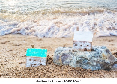 Close up of Two Wooden houses model on the rock and sand with soft wave from seascape background, Christian concept wise man build house on the rock but foolish man built house on the sand