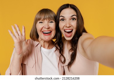 Close up two young excited smiling happy daughter mother together couple women wearing casual beige clothes do selfie shot pov on mobile phone waving hands isolated on plain yellow background studio