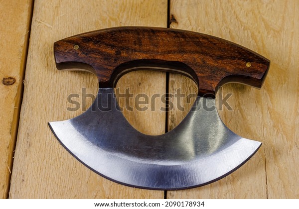 Close up of a Ulu knife with a wood handle on pine\
boards. Traditionally used by Inuit (Eskimo) women and is an\
all-purpose knife. \
