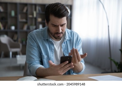 Close up unhappy dissatisfied businessman looking at phone screen, reading bad news in message, confused young male having problem with broken or discharged device, data loss or software failure - Shutterstock ID 2045989148