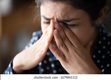 Close up unhappy Indian girl crying, touching nose bridge, exhausted sad woman suffering from strong headache migraine or panic attack, feeling unwell, emotional stress, mental disorder