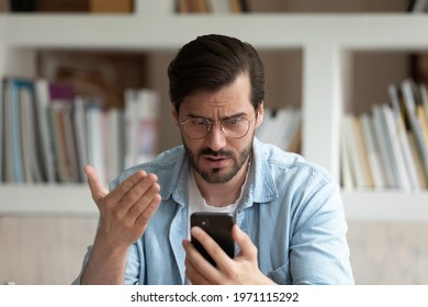 Close up unhappy irritated man in glasses looking at phone screen, worried businessman reading bad news in message, confused young male having problem with broken or discharged device, data loss - Shutterstock ID 1971115292