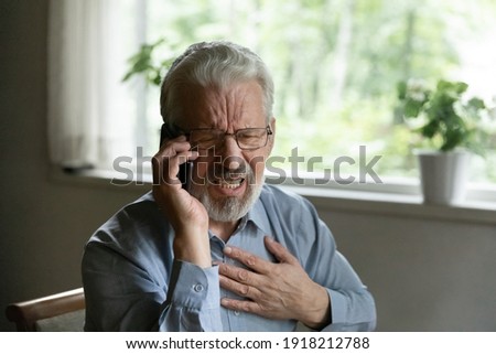 Close up unhappy mature man wearing glasses touching chest, calling emergency, having heart attack, frustrated elderly male hearing bad news, suffering from heartache disease, feeling pain