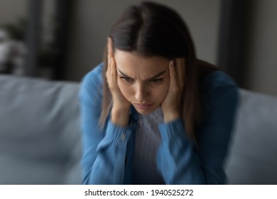 Close up unhappy woman suffering from strong headache and dizziness, depressed young female blurry motion background, sitting on couch alone, touching temples, feeling pain, unwell and unhealthy - Shutterstock ID 1940525272