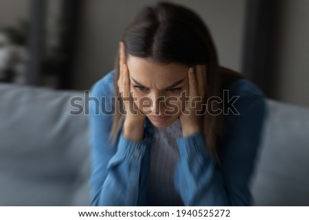 Close up unhappy woman suffering from strong headache and dizziness, depressed young female blurry motion background, sitting on couch alone, touching temples, feeling pain, unwell and unhealthy