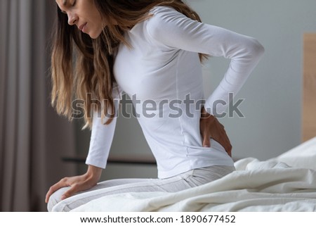 Close up unhappy woman wearing pajama rubbing stiff back muscles after awakening, sitting on bed, upset young female feeling pain, incorrect posture or uncomfortable bed, backache after sleep
